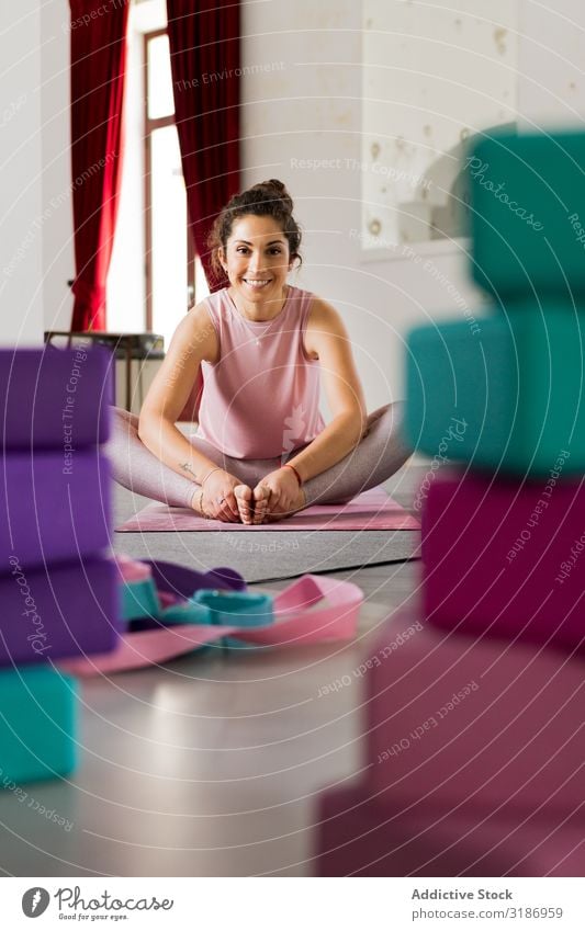 Frau, die zwischen den Sportgeräten im Studio sitzt. Gerät Studioaufnahme Yoga sitzen brünett dünn Unterlage Sportbekleidung rosa mehrfarbig attraktiv beweglich