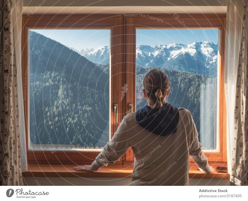 Anonyme Frau, die aus dem Fenster auf Berge schaut. Berge u. Gebirge bewundernd anlehnen Fensterbrett heimwärts Sonnenstrahlen Tag Unbekümmertheit Natur