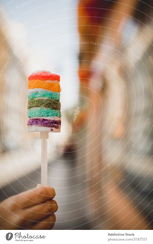 Hand hält köstlichen Regenbogenkuchen auf der Stadtstraße. Lebensmittel Wüste Kuchen mehrfarbig hell Süße Mahlzeit Ernährung Fressen geschmackvoll lecker