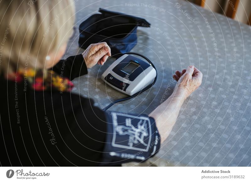Ältere Frau, die den Blutdruck misst. Druck Messung Bildschirm elektronisch modern alt heimwärts Tisch Prüfung & Examen Gesundheit Routine Senior reif