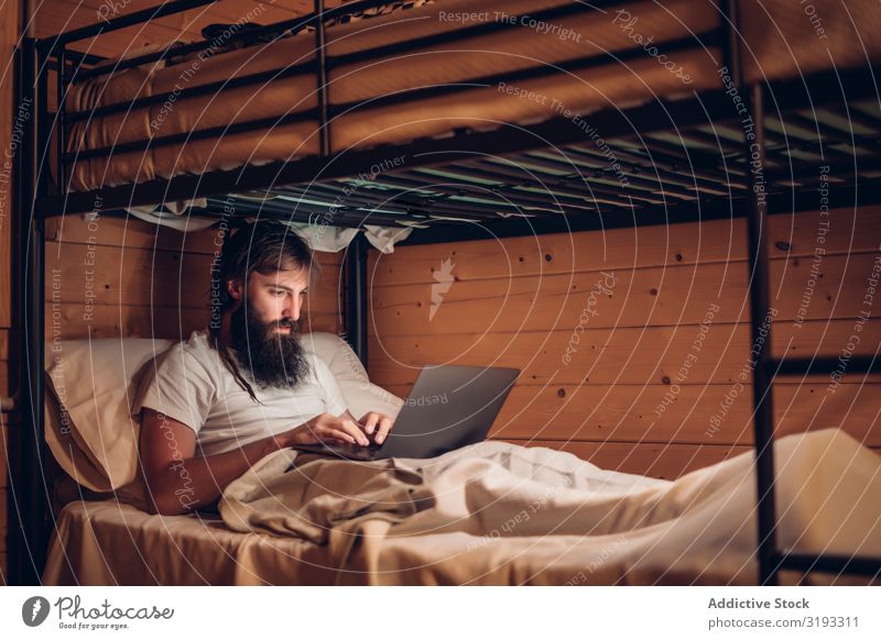Mann mit Laptop im rustikalen Etagenbett Notebook benutzend Schickimicki Arbeit & Erwerbstätigkeit freiberuflich bärtig Holz Haus konzentriert
