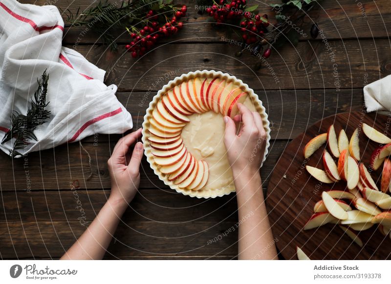 unkenntliche Frau, die einen Apfelkuchen auf einem Holztisch macht. Pasteten frisch rustikal Fenster gebastelt Tag braun Konfekt organisch Pergament Wärme