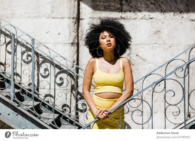 Stylische ethnische Frau, die sich auf ein Geländer im Freien stützt. glamourös Stil trendy modisch Haare & Frisuren Afro-Look Freizeit & Hobby Jugendliche