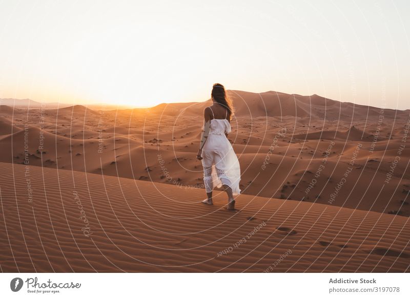 Frau in weißem Kleid, die in der Wüste spazieren geht. Sonnenuntergang Sand Marokko weißes Kleid Natur Sommer abgelegen Ferien & Urlaub & Reisen fliegendes Haar