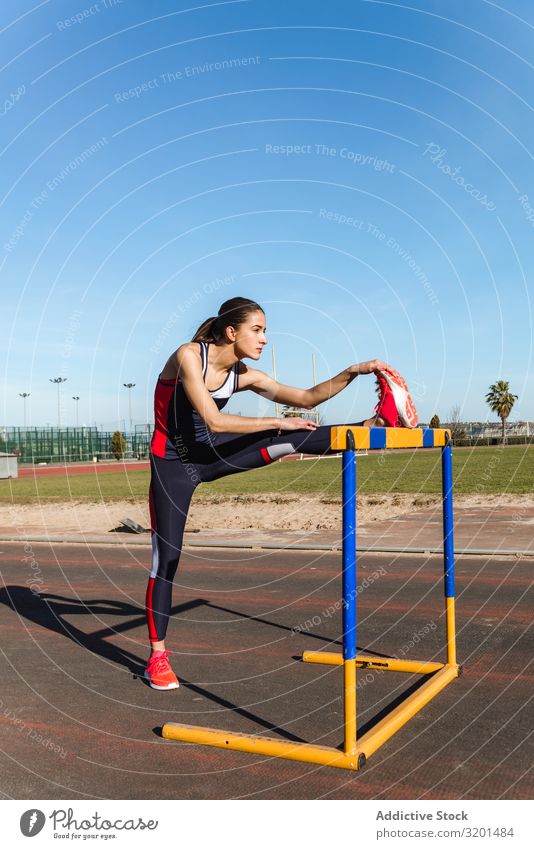 Athletin beim Stretching auf der Hürde im Stadion Frau strecken Dehnung verlängern Sport Bahn Jugendliche Sportbekleidung Himmel blau Konkurrenz springen