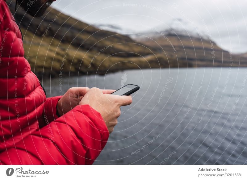 Anonymer Mann mit Smartphone in der Nähe eines Sees auf den Färöern Fluss grün Mensch weiß Telefon Halt vorbei Handy Nachrichtenübermittlung Mitteilung klug