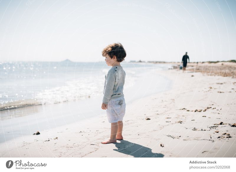 Barfüßiges Kind in kurzen Wellen am Sandstrand klein winken Strand Barfuß Säuglingsalter niedlich Freude erkundend schön heiter Kindheit Fundstück hübsch