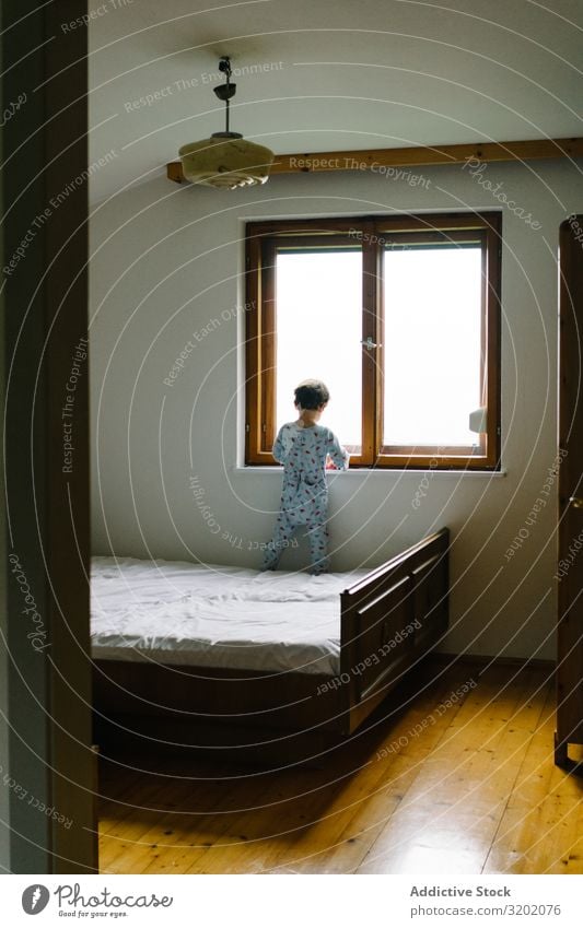 Kind im Schlafanzug steht auf dem Bett und schaut aus dem Fenster Pyjama Schlafzimmer Freizeit & Hobby heiter Lifestyle Genuss beobachten reizvoll schön