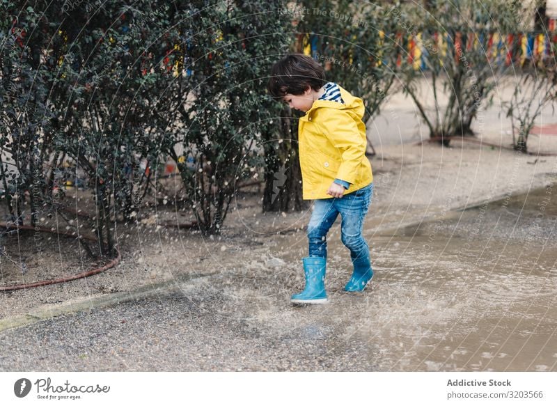 Glückliches Kind springt auf Pfütze Junge springen Freude Straße Gummistiefel nass Wasser spielerisch Kindheit Herbst Wetter Natur Spielen Regenmantel