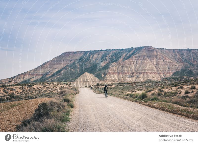 Mann fährt Fahrrad auf der Straße in den Wüstenhügeln Hügel Landschaft Sand Stein Pflanze Ausflug regenarm Natur Himmel Ferien & Urlaub & Reisen heiß
