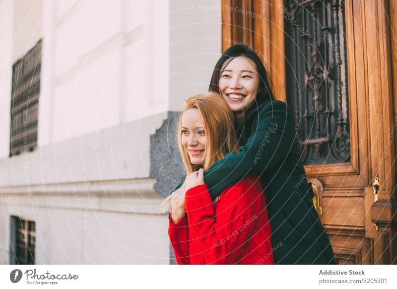 Fröhliche Freundinnen umarmen sich in der Nähe einer Ziertür Freundschaft Umarmen Lächeln Wegsehen Tür Straße Gebäude Großstadt Person gemischter Abstammung
