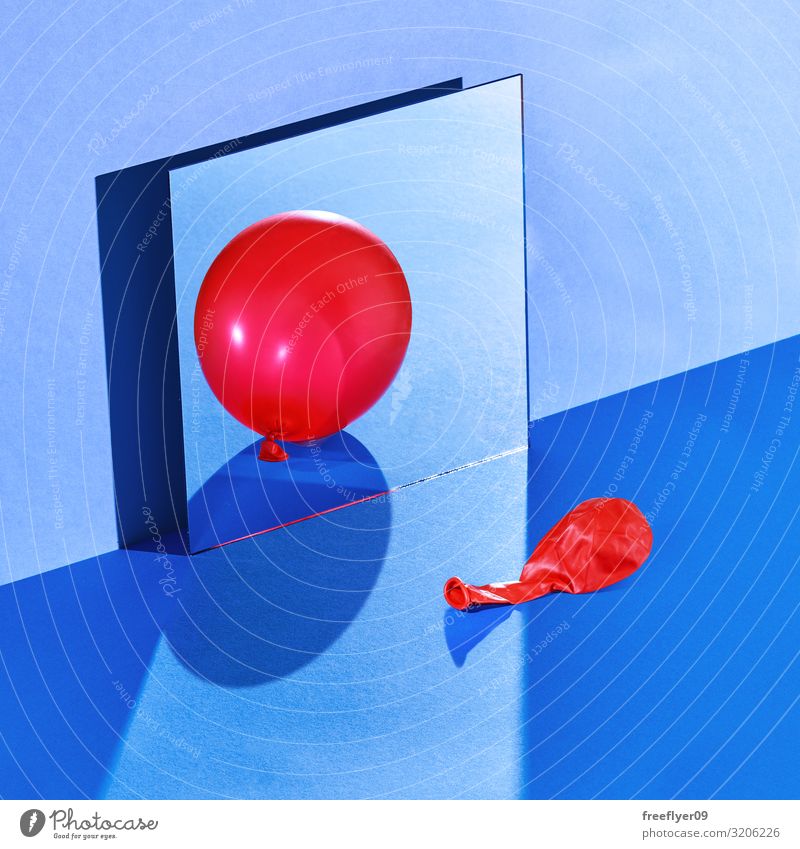 Ein Ballon, der sich mit einer falschen Reflexion reflektiert. Tisch Spiegel Mode Luftballon glänzend blau rot Stillleben hart Licht Wand Quadrat