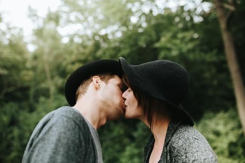 junges heterosexuelles Paar mit Hüten, das sich küsst Zuneigung Bonden lässig Kaukasier charmant niedlich Termin & Datum Datierung Tag tagsüber emotional