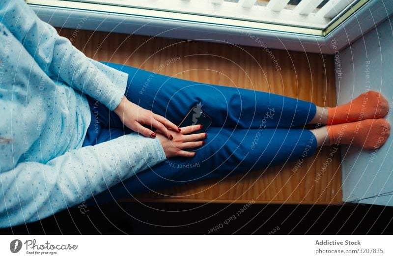 Getreidefrau in Hauskleidung auf dem Fensterbrett Frau Komfort heimwärts gemütlich Smartphone farbenfroh Schottland Sitzen sich[Akk] entspannen Lifestyle