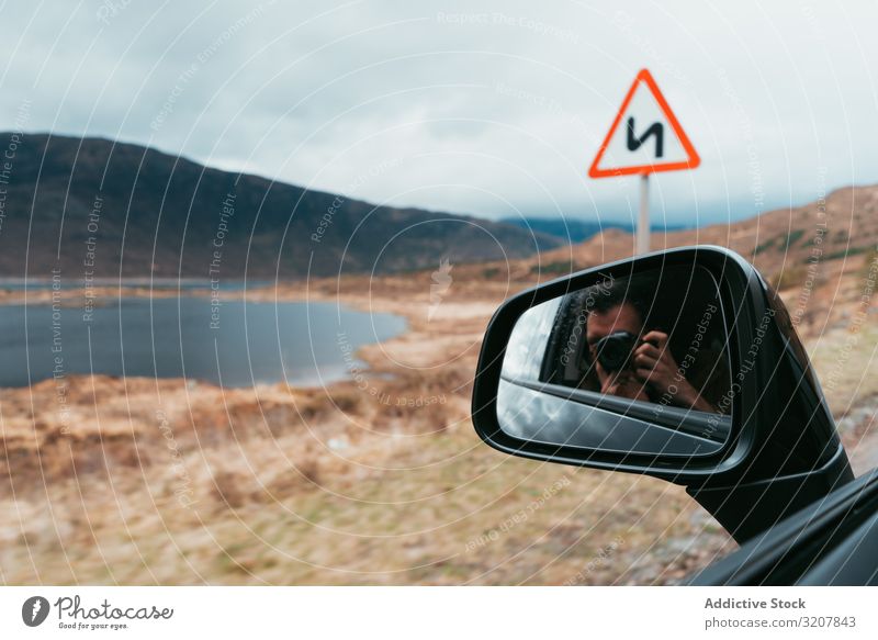 Reisefotograf mit Kamera im Auto Mann reisen Fotografie PKW Spiegel Landschaft Schottland Fotokamera Selbst Verkehr See Berge u. Gebirge abgelegen Automobil
