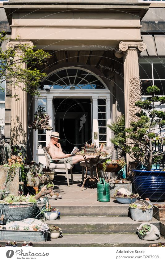 Mann auf der Veranda mit dekorativen Pflanzen im Sonnenlicht Schottland Lifestyle Zeitung Freizeit lesen Design Gartenarbeit Dekoration & Verzierung wohnbedingt