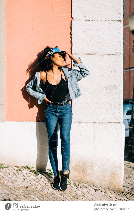 Hübsche ethnische Frau, die an der Wand lehnt und den Kopf hält Mode stylisch trendy Bekleidung glamourös Outfit Stirnband Jeanshose Jeansstoff jung