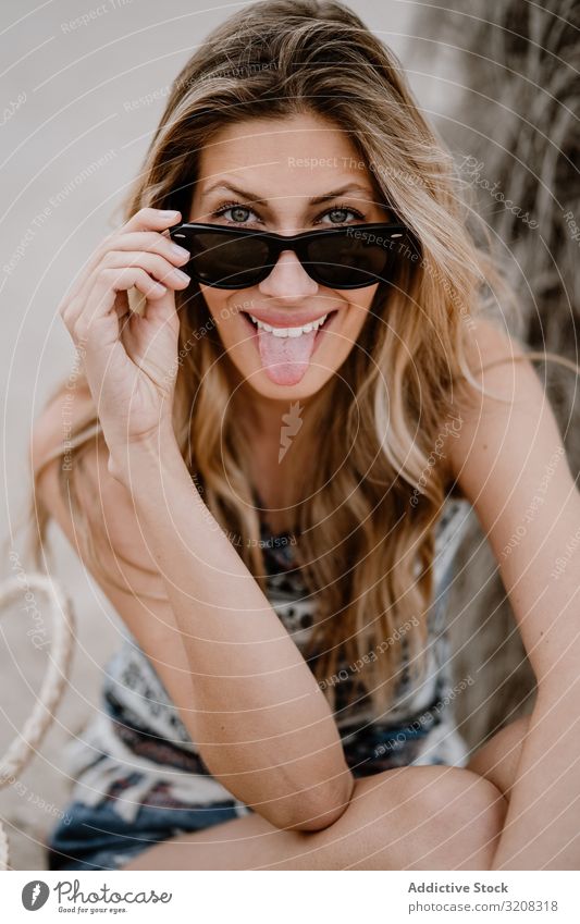Porträt einer jungen fröhlich-schönen Frau mit Sonnenbrille Strand herausstechend Zunge modisch lustig glamourös Grimasse spielerisch Sommer Urlaub reisen