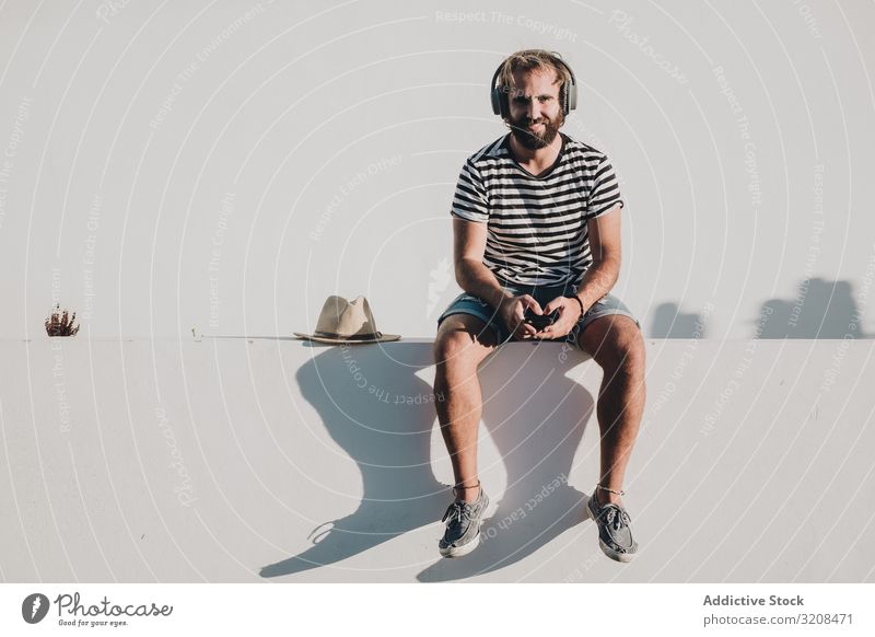 Junger Mann sitzt mit Smartphone und Kopfhörern Musik reisen Urlaub Feiertag la restinga Kanarische Insel El Hierro benutzend Sommer jung männlich Person lässig