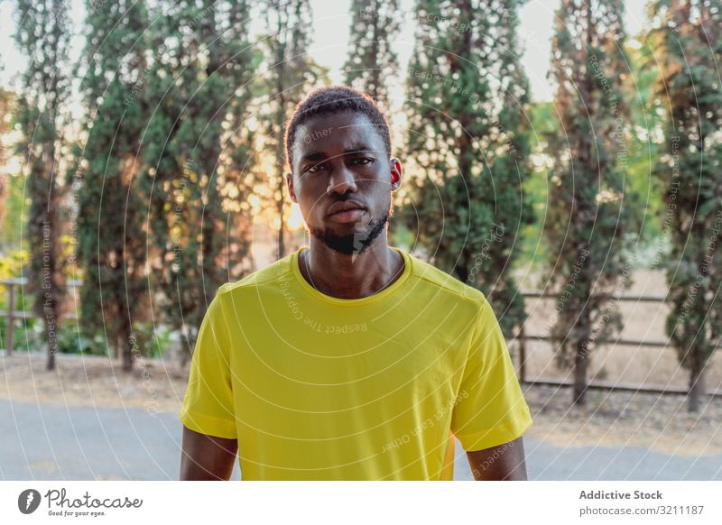 Schwerer schwarzer Mann steht beim Joggen im Park entschlossen Sport Porträt Sonnenlicht cool selbstbewusst ethnisch Afroamerikaner männlich Training Athlet
