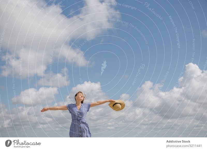 Fröhliche junge Frau genießt die Brise genießend Glück sorgenfrei Freiheit Wind Sonnenkleid Sommer Spaziergang fliegendes Haar Windstille Strohhut positiv