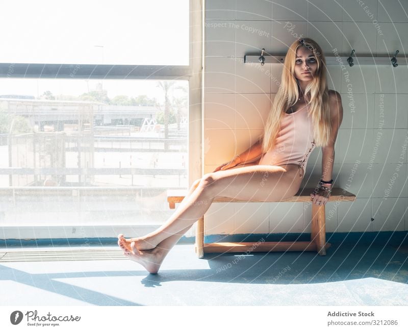 Junge Frau in der Umkleidekabine eines Schwimmbades Ankleidezimmer Pool Badebekleidung Fitness sinnlich Bank sitzen jung Sonnenlicht sportlich Fenster Barfuß
