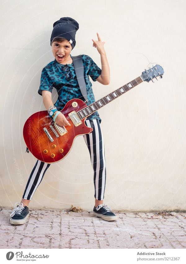 Energisches Kind gestikulierend Rock haltend Gitarre Junge Spielen Rockstar Felsen farbenfroh Kindheit Mode Zeichen Künstler Musiker festlich Lachen wenig
