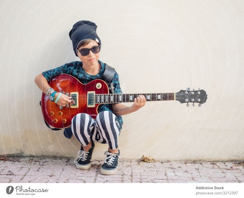 Energisches Kind hält Gitarre Junge Spielen Rockstar Felsen farbenfroh Kindheit Mode Zeichen gestikulieren Künstler Musiker festlich Lachen wenig Zeitgenosse