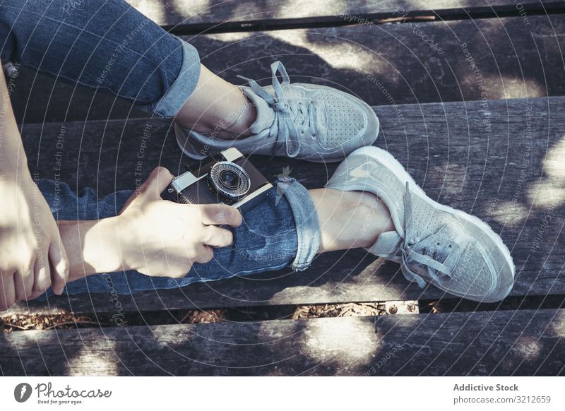 Auf Bank sitzende Frau mit gekreuzten Beinen Fotokamera blau Sport trendy modern Schuhe Fotografie strecken bequem Turnschuh Erholung Fuß kreativ Hipster