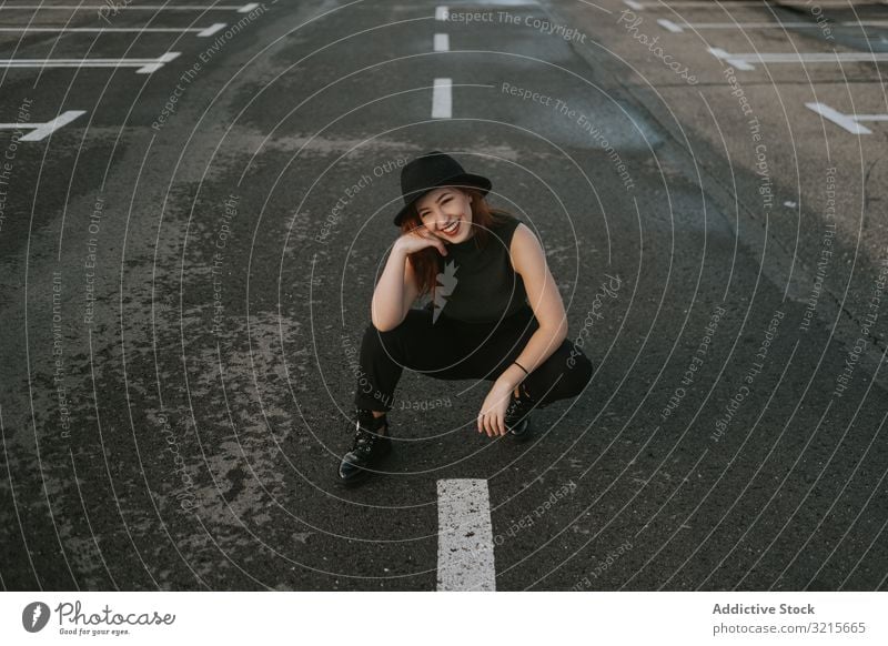 Lächelnde Frau sitzt auf Straße mit Markierungen attraktiv leer Aufschlag stylisch Mode jung Warten Glück Regie Model elegant Lifestyle schön Abenteuer trendy