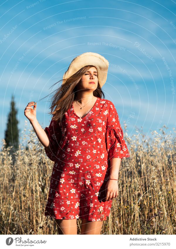 Glückliche verträumte Frau steht im hohen Gras Feld attraktiv Lächeln Strohhut rotes Kleid blau Himmel Natur Sommer jung Lifestyle positiv Fröhlichkeit charmant