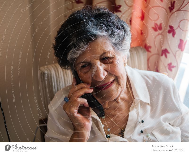 Fröhliche ältere Frau telefoniert zu Hause mit dem Handy gealtert sprechend heimwärts Großmutter Erfahrung Weisheit modern Gespräch Aufmerksamkeit Großeltern
