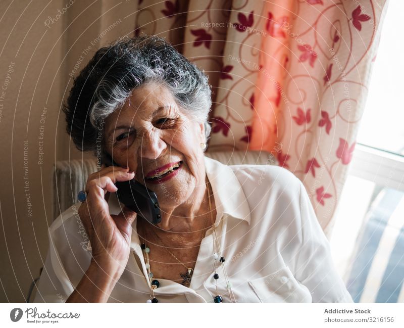 Fröhliche ältere Frau telefoniert zu Hause mit dem Handy gealtert sprechend heimwärts Großmutter Erfahrung Weisheit modern Gespräch Aufmerksamkeit Großeltern
