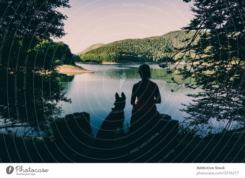 Frau mit Hund ruht sich am schönen See aus Silhouette aussruhen bewundernd Reisender Tourismus wandern malerisch Wald Sommer Tag Haustier Tier Freundschaft