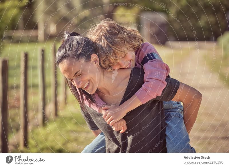 Lächelnde Mutter hält bezaubernden Sohn auf dem Rücken Landschaft freudig Stehen Glück Kind wenig heiter Zusammensein Elternschaft Kindheit Spaß lässig Natur