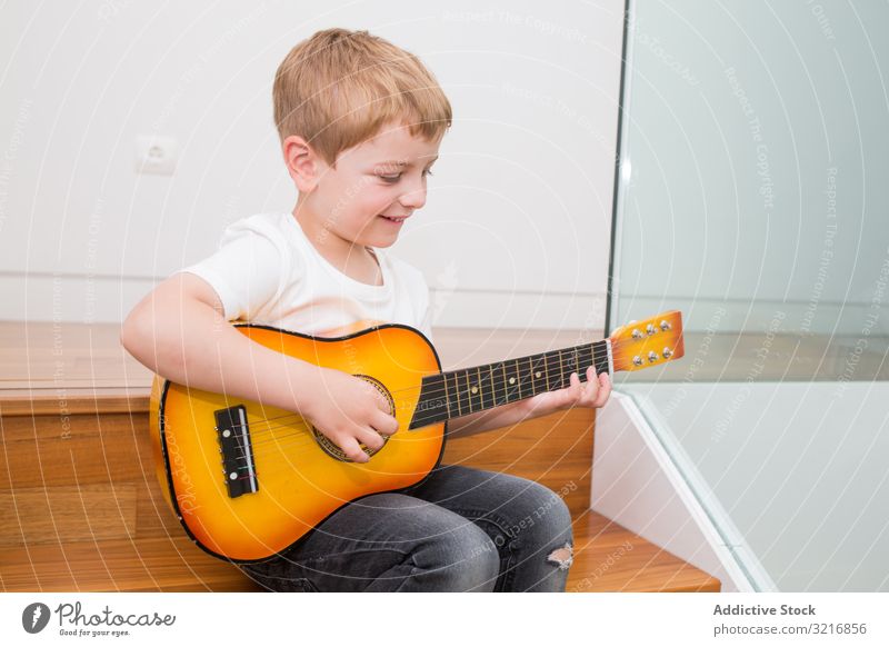 Junger blonder Junge spielt Spielzeuggitarre Gitarre Spielen Musik Instrument Kind Hobby Musiker talentiert wenig männlich lässig niedlich bezaubernd