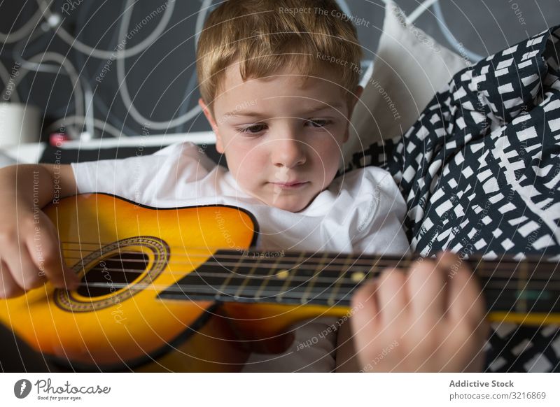 Junger blonder Junge spielt Spielzeuggitarre Gitarre Spielen Musik Instrument Kind Hobby Musiker talentiert wenig männlich Person lässig niedlich bezaubernd