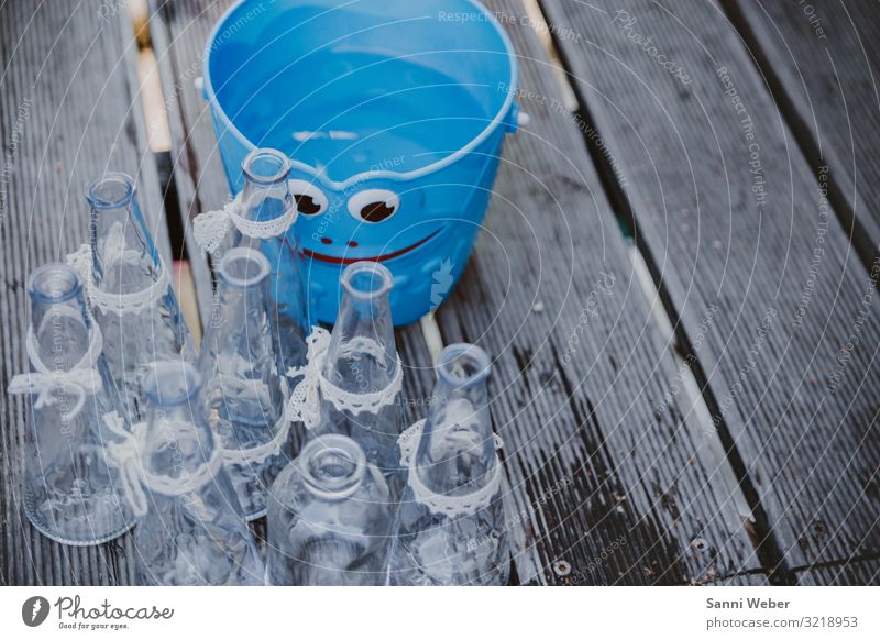 Blauer Eimer mit Gesicht Kunststoff Glück Glas Flasche Schleifenband weiß Holz Bodenbelag nass Farbfoto mehrfarbig Außenaufnahme Nahaufnahme Textfreiraum rechts