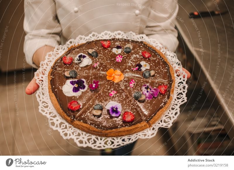 Brauner, mit Blumen geschmückter Kuchen in Frauenhänden Pasteten selbstgemacht süß Bäckerei Feinschmecker organisch Ernährung geschmackvoll appetitlich Hände
