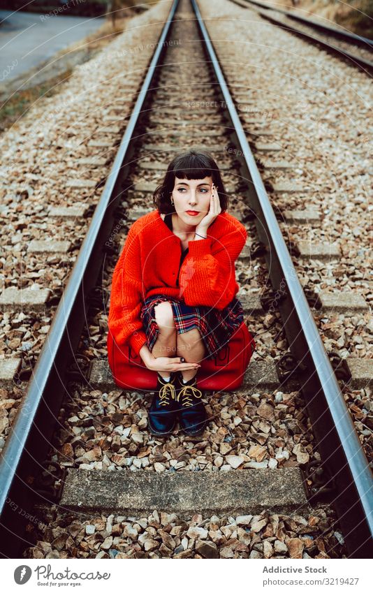 Frau sitzt auf Schwellen in der Mitte der Eisenbahn Koffer rot reisen stylisch grün Gepäck Natur schön Tasche Warten Freiheit Straße allein Ausflug Reise Buchse