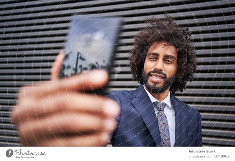 Fröhlicher ethnischer Mann, der Egoismus nimmt und lächelt modern Geschäftsmann formal Afrikanisch schwarz Smartphone Selfie Wand Lächeln Glück Afro-Look heiter