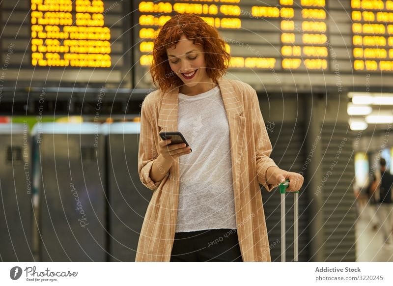 Rothaarige junge Frau benutzt Smartphone am Bahnhof Station reisen Business Urlaub Lächeln Tourist Eisenbahn Abheben Koffer Passagier Terminal Warten Zeitplan
