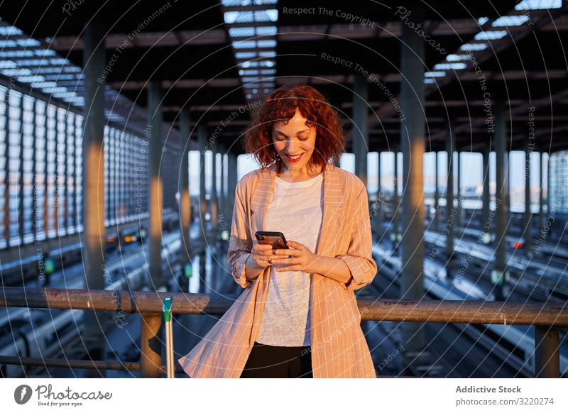 Lächelnde junge Frau beim Telefonieren am Bahnhof Eisenbahn Smartphone Anruf reisen Station Business Urlaub Tourist Mitteilung Terminal Abheben Koffer Abend