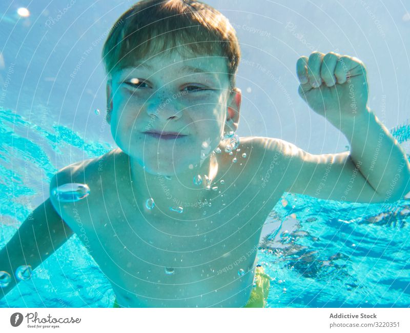 Lustiger Junge schwimmt unter Wasser und schaut in die Kamera schwimmen Pool lustig Grimasse Atem Halt Kind heiter spielerisch Sommer Kindheit Sinkflug