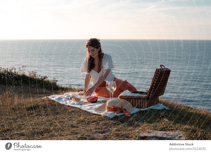 Frau mit Glas Getränk auf Picknickmatte in der Nähe von Meer und Bergen Seeküste Strand Sommer lesen Freizeit Himmel MEER sich[Akk] entspannen trinken Urlaub