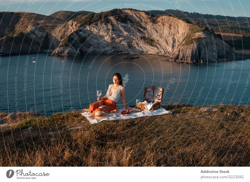 Frau mit Glas Getränk auf Picknickmatte mit Blick auf Meer und Berge Seeküste Strand Sommer lesen Freizeit Himmel MEER sich[Akk] entspannen trinken Urlaub