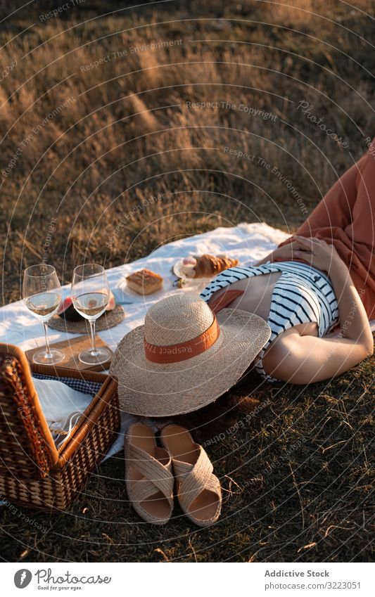 Frau ruht sich auf der Wiese auf Picknick aus und bedeckt Gesicht mit Hut Sommer Freizeit sich[Akk] entspannen Glas trinken Urlaub Sommerzeit altehrwürdig Mode