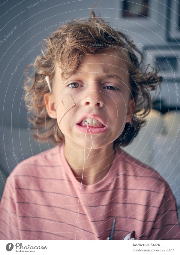 Kind mit Zahnseide im Gesicht und ermüdender Milchzahn zum Herausziehen Kindheit mündlich melken Mund dental offen zeigend Ausdruck heiter lustig