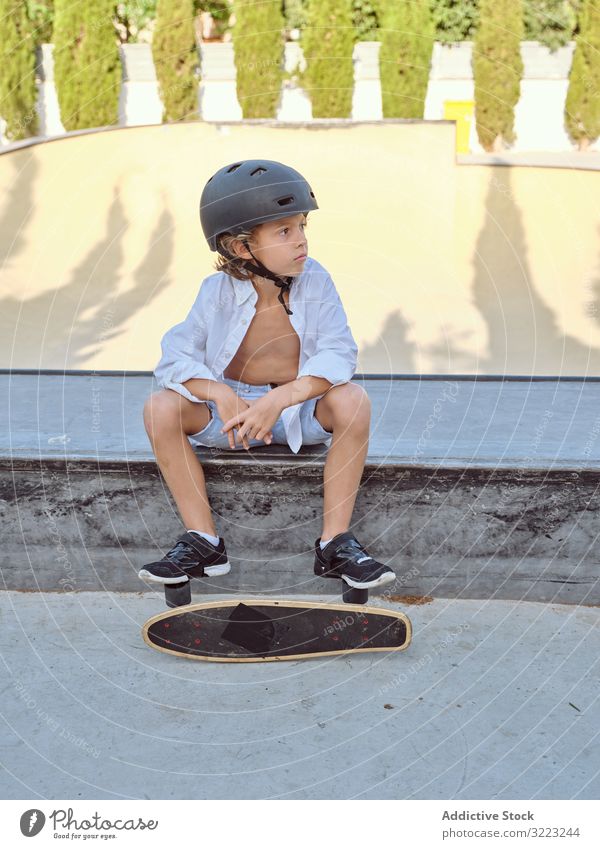Junge mit Skateboard auf Rampe sitzend Skatepark Schutzhelm Lifestyle Holzplatte Sitzen Sport Freizeit Hobby männlich jung Kindheit Sommer sonnig vorsichtig