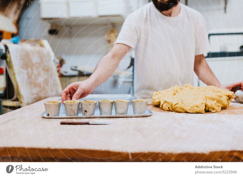 Bärtiger Konditor legt Teig in Tasse Bäckerei Teigwaren setzen Tisch Küche Gebäck Vorbereitung frisch Mann roh professionell Lebensmittel Küchenchef Restaurant